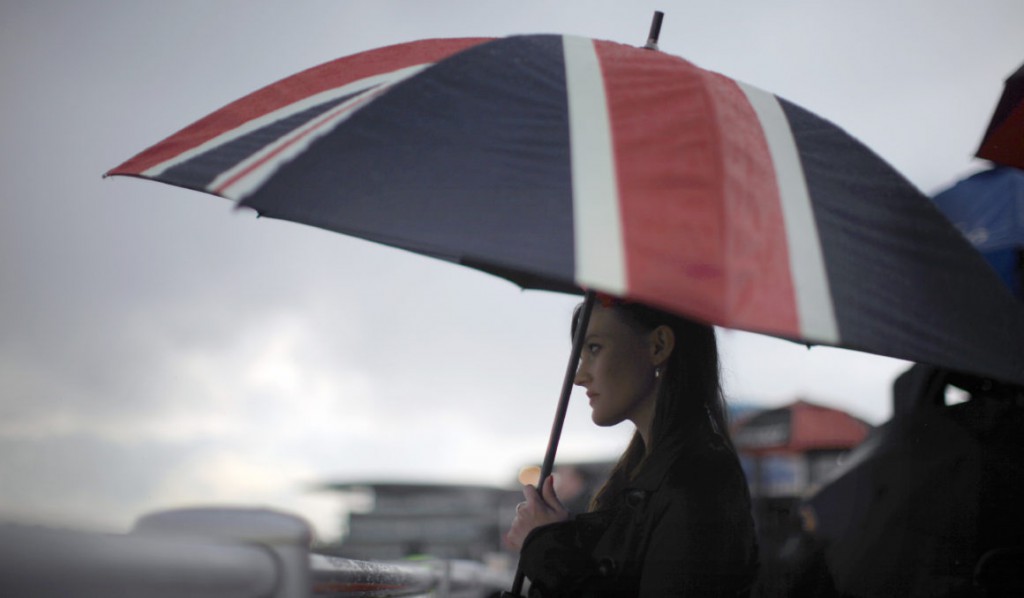 LIVERPOOL, ENGLAND - APRIL 13: A racegoer shelters from the rain under a large Union Jack umbrella during Ladies Day at the Aintree Grand National meeting on April 13, 2012 in Aintree, England. Friday is traditionally Ladies day at the three-day meeting of the world famous Grand National, where fashion and dressing to impress is as important as the racing. (Photo by Christopher Furlong/Getty Images)