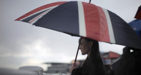 LIVERPOOL, ENGLAND - APRIL 13:  A racegoer shelters from the rain under a large Union Jack umbrella during Ladies Day at the Aintree Grand National meeting on April 13, 2012 in Aintree, England. Friday is traditionally Ladies day at the three-day meeting of the world famous Grand National, where fashion and dressing to impress is as important as the racing.  (Photo by Christopher Furlong/Getty Images)